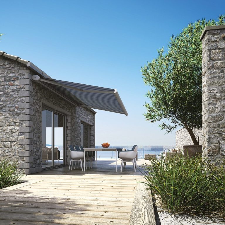 zu sehen ist eine Terrasse an einem Natursteinhaus und einer ausgefahrenen Markise von dem Hersteller Kadeco